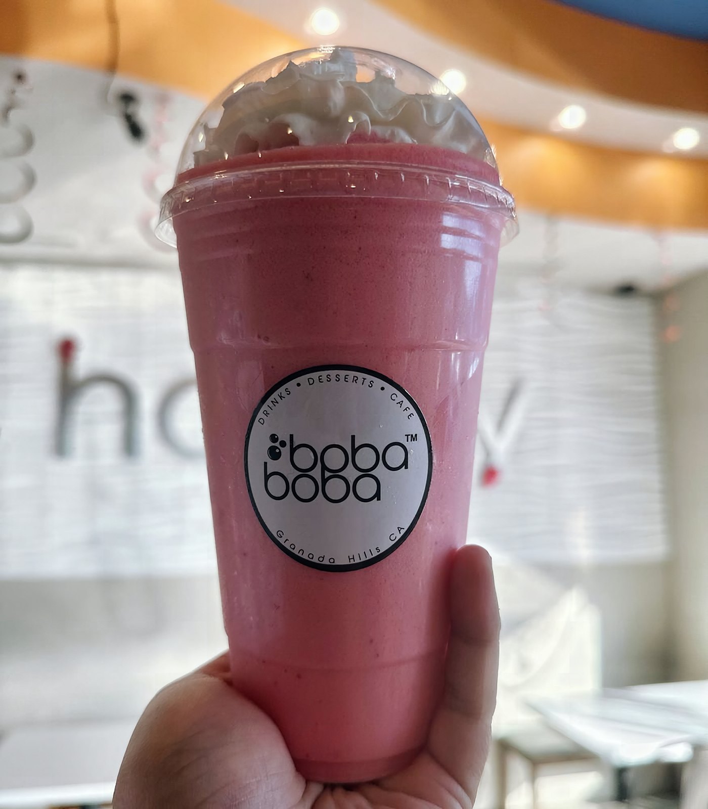 Pink strawberry shake with whipped cream under a dome lid, held up in the shop